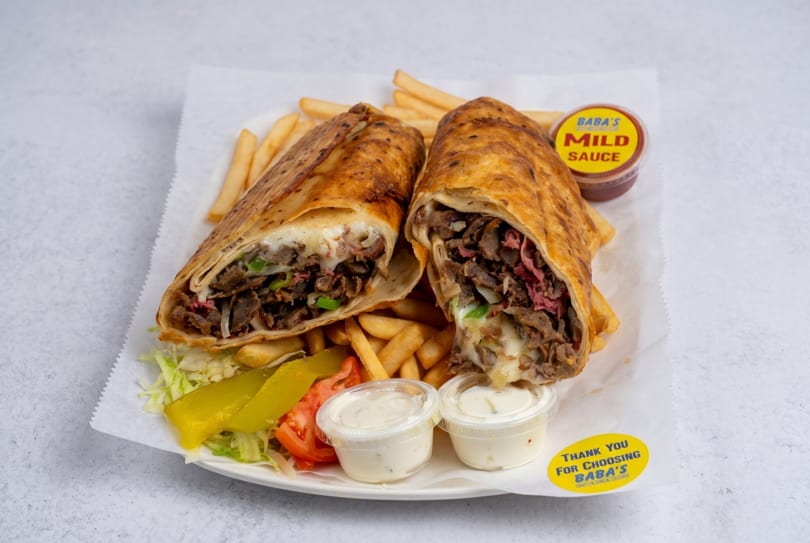 Two Baba's shawarma wraps, fries, salad, and sauces on a white plate.