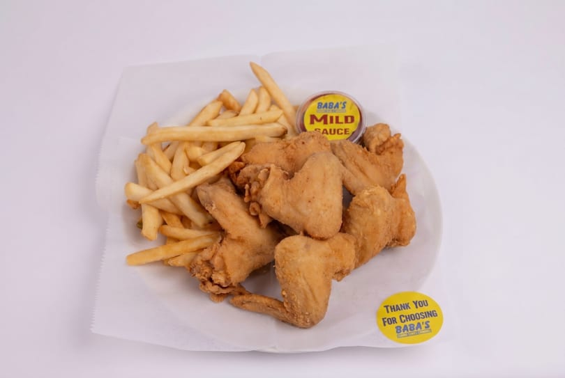 Fried chicken wings and french fries with Baba's Mild Sauce on a white plate.