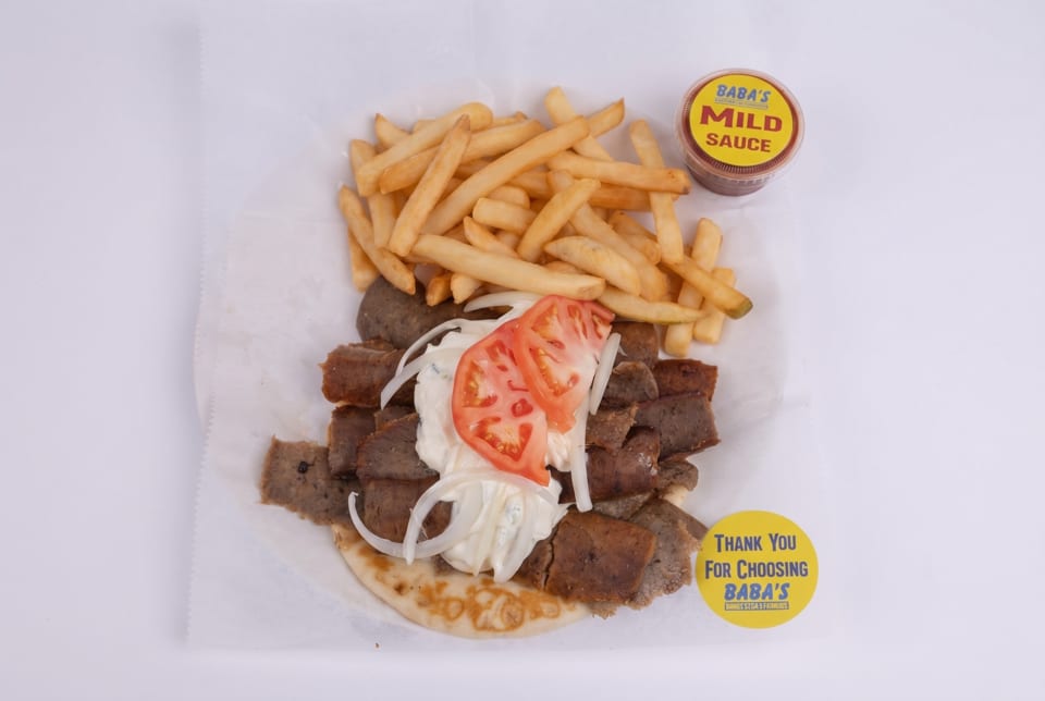 Baba's gyro platter with meat, tomatoes, onions, sauce, and fries, plus a side of mild sauce.