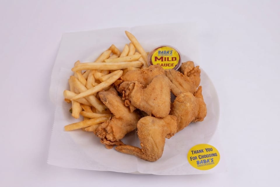 Baba's fried chicken wings and french fries with a side of mild sauce on a white plate.