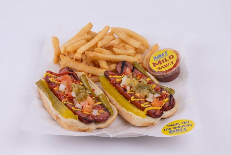 Two Baba's hot dogs with fries and a side of mild sauce on a white paper tray.